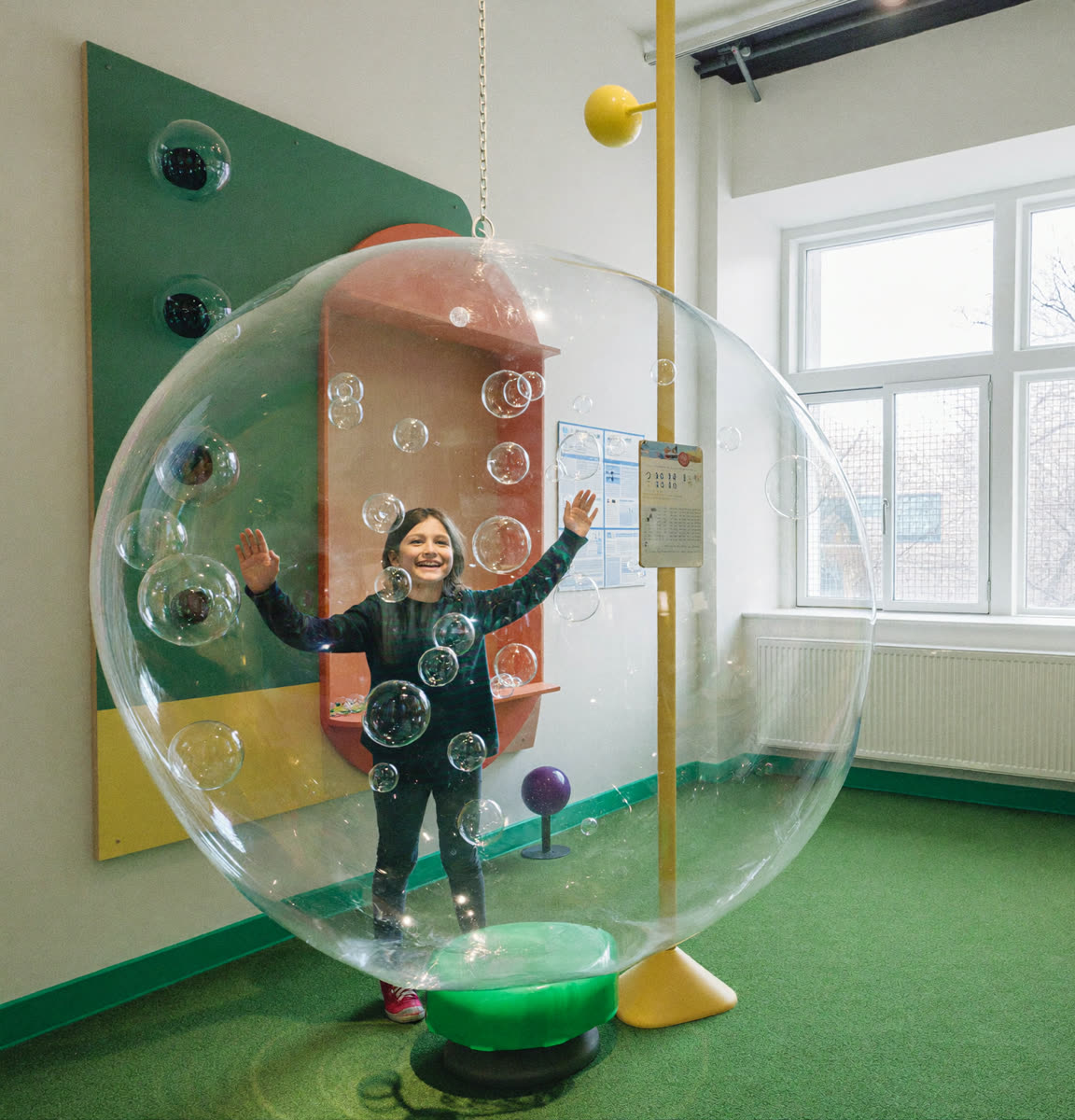 A delighted child standing inside a giant shimmering soap bubble at Bubble-ology