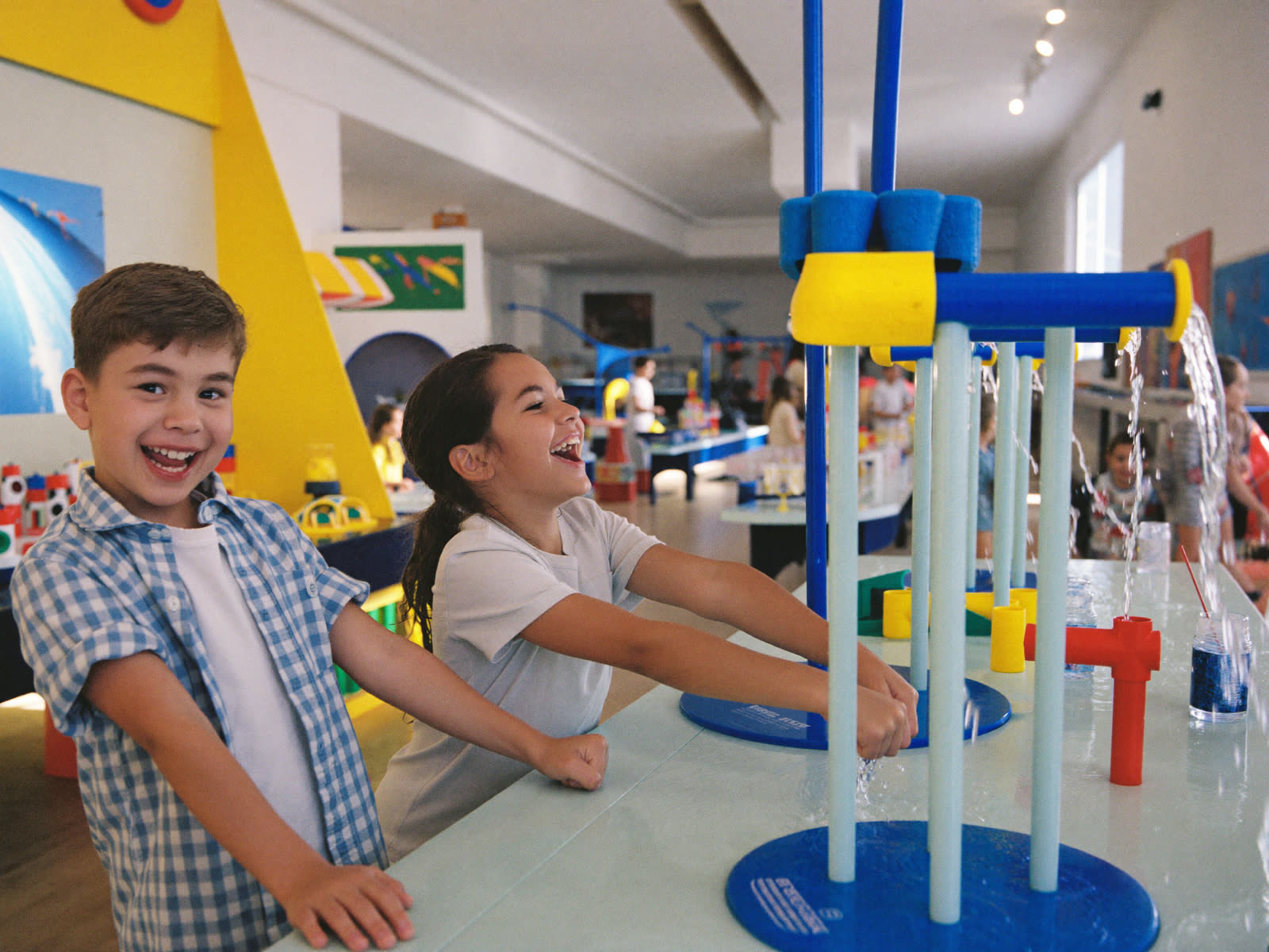 Two kids laughing while steering water through flumes at the Water Works table