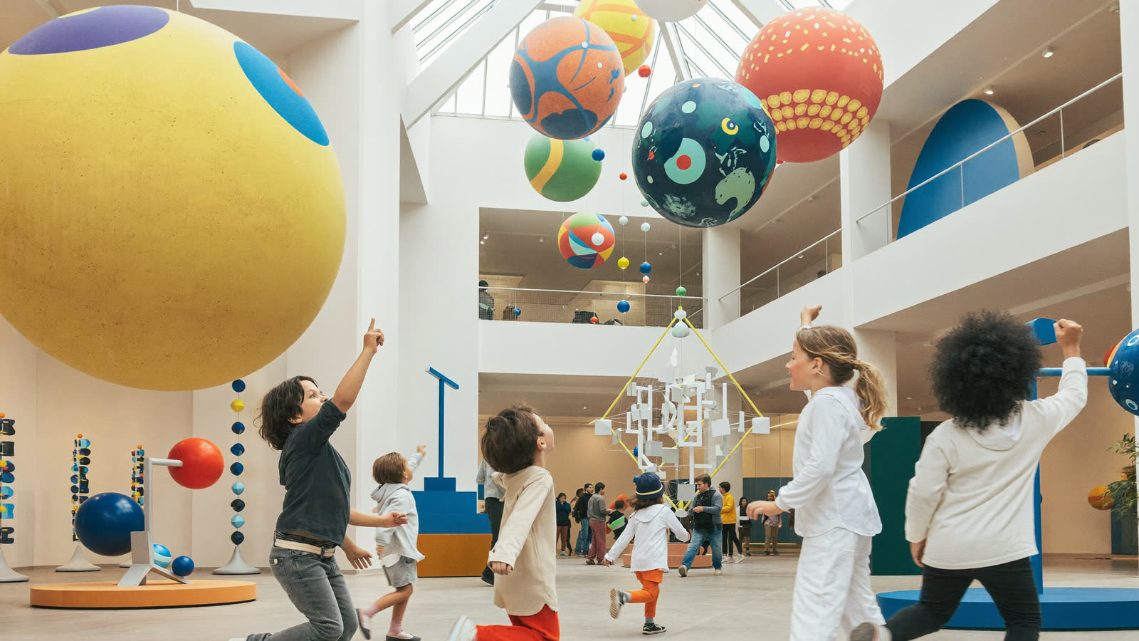 Kids pointing up in wonder at giant hanging planets in the bright Curio atrium