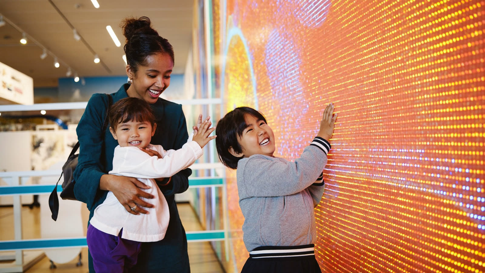A parent and two kids laughing together at a glowing interactive light wall
